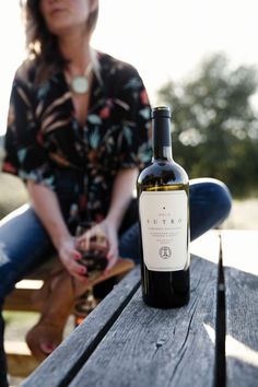 a woman sitting on a picnic table with a bottle of wine in front of her