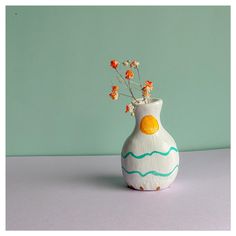 a white vase with orange flowers in it on a gray table next to a green wall