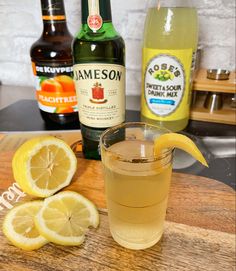 a wooden cutting board topped with a glass filled with liquid and sliced lemons next to bottles