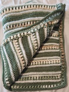 a green and white crocheted blanket laying on top of a bed next to a pillow