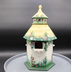 a decorative birdhouse with flowers painted on it's sides and a yellow roof