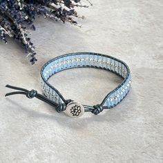 A Hematite stacker bracelet on soft silver leather, combined with pastel blue beads and finished off with a silver TierraCast lotus flower button. A perfect gift for a loved one or simply a treat for yourself! ✨ - Measures 17cm/6.75"  - Has one extra loop which adds another 2.5cm/1" if needed (if not needed the loop can be carefully cut off, leave a 1.5cm tail) - Soft silver leather - 3mm round silver Hematite - 3mm faceted Czech glass - Jewellery grade thread - Silver TierraCast lotus flower button Hematite: Protects, stabilises and grounds. Increases confidence, clarity and mental organisation. Shifts negative energy out of the aura (Root Chakra). This piece comes in an organza bag and wrapped in tissue, ready to give 💕 https://www.etsy.com/uk/shop/LittleGemsbyMel For real life events a Elegant Adjustable Blue Leather Bracelet, Elegant Blue Adjustable Leather Bracelet, Adjustable Hand Wrapped Blue Leather Bracelet, Elegant Blue Leather Bracelet For Gift, Adjustable Blue Wrap Bracelet For Everyday, Blue Beaded Leather Bracelet For Gift, Adjustable Silver Wrap Bracelet With Round Beads, Adjustable Silver Spiritual Wrap Bracelet, Silver Wrap Bracelet With Adjustable Round Beads