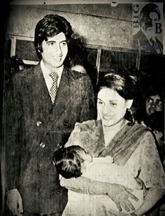 an old black and white photo of a man holding a baby while standing next to a woman