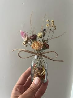 a hand holding a glass jar with dried flowers in it and a ribbon tied around the top