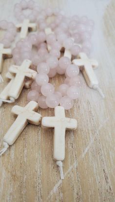 some white and pink beads are laying on a wooden surface with crosses in the middle