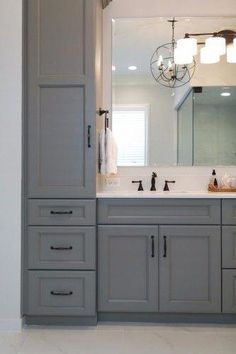 a bathroom with gray cabinets and white counter tops is pictured in this image, there are lights hanging above the sink