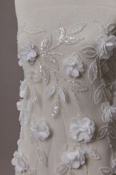 the back of a wedding dress with white flowers and pearls on it's side