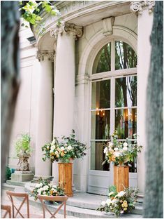 two wooden chairs sitting in front of a building with flowers on the windowsills