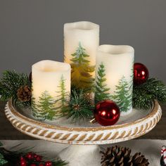 three lit candles sitting on top of a platter filled with pine cones and christmas decorations