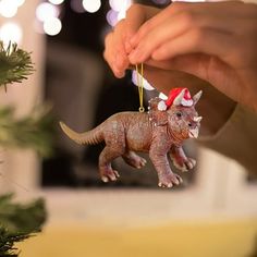 a hand holding a christmas ornament with a small dinosaur on it's back