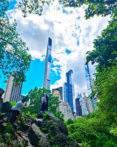 people are standing on rocks in the middle of a park with skyscrapers in the background