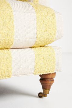 a yellow and white striped chair with wooden legs on a white floor, next to a pillow