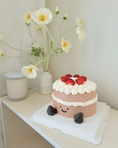 a cake with strawberries on top sitting on a table next to flowers and a vase