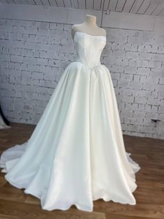 a white wedding dress is on display in front of a brick wall and wooden floor