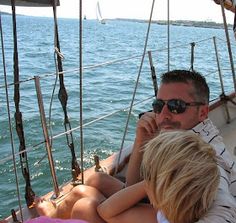 a man and two children are sitting on a sailboat in the water while looking at something