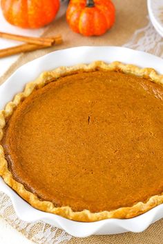 a pie sitting on top of a white plate next to pumpkins and cinnamon sticks