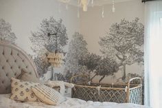 a bedroom with a bed, chandelier and wallpapered trees on the walls