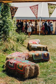 some hay bales sitting in the grass with people standing around them and flags flying overhead