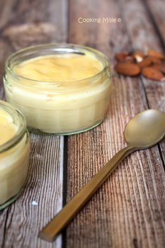 two small jars filled with pudding sitting on top of a wooden table next to a spoon