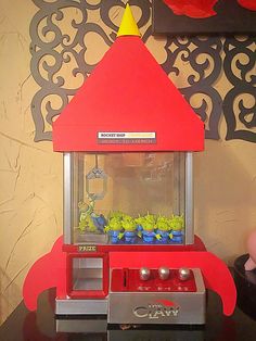 a red toy machine with plants in it on a black table next to a wall