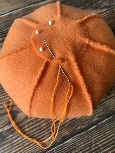 an orange hat with two pins on it sitting on top of a wooden table next to some thread