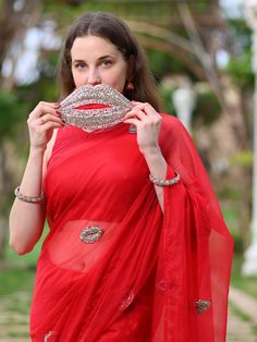 This is a three-piece red lip saree set from the Ensembles collection. The red lip saree is paired with a red sleeveless blouse. The blouse has a round neckline. There are beautiful lip motifs of shimmer cutdana work all over the saree. This saree set is crafted in semi pure organza fabric. The outfit is completed with a heavily embellished, cutdana work shimmer lip shape handbag. Elegant Red Pre-draped Saree For Puja, Red Pre-draped Saree With Mirror Work For Evening, Red Pre-draped Saree With Mirror Work For Party, Elegant Saree With Mirror Work For Puja, Indo Western Saree, Baby Pink Saree, Pant Saree, Yellow Drapes, Black Embroidered Blouse