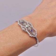 This is part of Chairish’s Fine Jewelry assortment.  A delicate Art Deco bracelet made of 14k white gold with a European cut diamond centre and two French cut sapphires on the side. The centrepiece has a symmetrical design, filled with delicate filagree and a scrolling foliate motif that is detailed and beautifully crafted. The diamond measures 4 mm and has .25 carat weight, it is G/H in colour and VS11 in clarity. The sapphires measure about 2.5 mm and have a well saturated blue tone. The centr Art Deco Jewelry Bracelet, Fine Jewelry With Sapphire And Single Cut Diamonds, Exquisite Silver Diamond Bracelet With Single Cut Diamonds, Formal Sapphire Jewelry With Single Cut Diamonds, Fine Jewelry White Gold Bracelets With Intricate Design, White Gold Bracelets With Intricate Design For Fine Jewelry, White Gold Bracelets With Intricate Design, Classic Sterling Silver Bracelet With Intricate Design For Wedding, White Gold Filigree Bracelet For Weddings