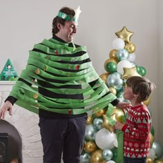 a man in a green christmas tree costume standing next to a little boy wearing a red sweater