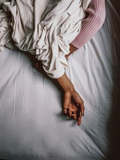 a woman laying on top of a bed covered in white sheets and blankets with her hand resting on the pillow