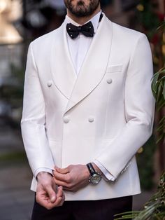 a man in a white tuxedo with a black bow tie and watch on his wrist