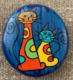 a painted button with a cat and kitten sitting on it's side, in the middle of carpeted area