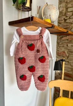 a baby's strawberry knitted outfit hanging on a clothesline next to a chair