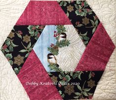 a quilted hexagon with two birds on it and holly leaves in the center