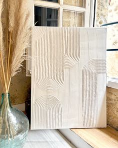 a vase with some dry grass in it next to a painting on a window sill