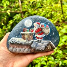 a hand holding up a rock with a santa clause painting on it