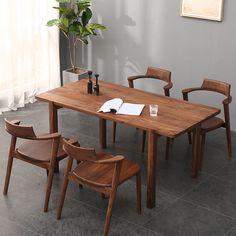 a wooden table with four chairs and a vase on the side, in front of a window