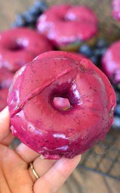 a person holding up a pink doughnut with blueberries on it