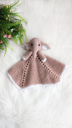 an elephant crocheted blanket laying on top of a white fur covered floor next to a plant