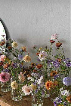 several vases filled with different types of flowers on top of a wooden table next to a mirror