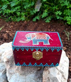 an elephant painted wooden box sitting on top of a rock