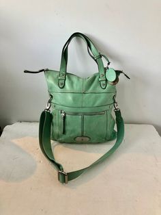 "sz X large width: 14\" height: 15\" side width 2\" TO 4\"  hand straps, length: 16\"crossbody strap 47\" x large pistachio green leather purse rich soft powder grain leather zip-top closure with a leather pull tab  a silver-tone metal logo badge one large exterior front zip pockets  a  stap closure large exterior back slip-in pocket two flat top handle straps extra long adjustable and removable web crossbody strap large inside compartment silver-tone metal key and hardware one inside zip compar Green Top Handle Satchel With Adjustable Strap, Green Top Handle Shoulder Bag With Adjustable Strap, Vintage Green Satchel With Double Handle, Green Vintage Satchel With Double Handle, Green Canvas Shoulder Bag With Handles, Vintage Green Double Handle Satchel, Green Satchel Shoulder Bag With Handles, Vintage Green Top Handle Shoulder Bag, Green Leather Hobo Bag With Top Carry Handle