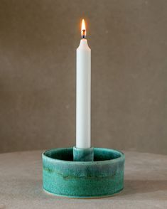 a single white candle is lit in a green cup