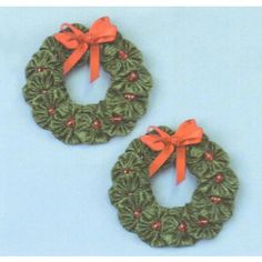 two green wreaths with red bows are on a blue background and one has an orange bow