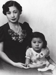 an old black and white photo of a woman holding a child in her lap, with another woman standing behind her