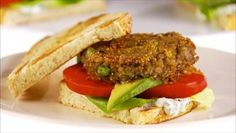 a sandwich with tomatoes, lettuce and meat on it sitting on a white plate