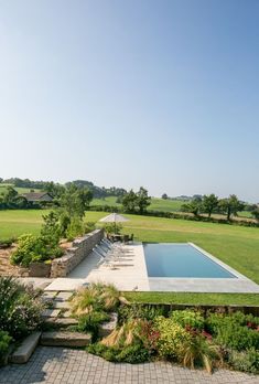 an outdoor swimming pool surrounded by greenery and stone walkways in the middle of a field