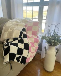 a vase with some plants in it next to a blanket on a couch near a window