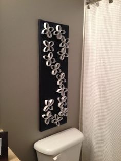 a white toilet sitting next to a black and white wall hanging on the side of a bathroom