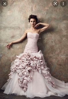 a woman in a pink dress leaning against a wall with her arms behind her head