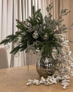 a silver vase filled with lots of snow covered plants and balls on top of a table